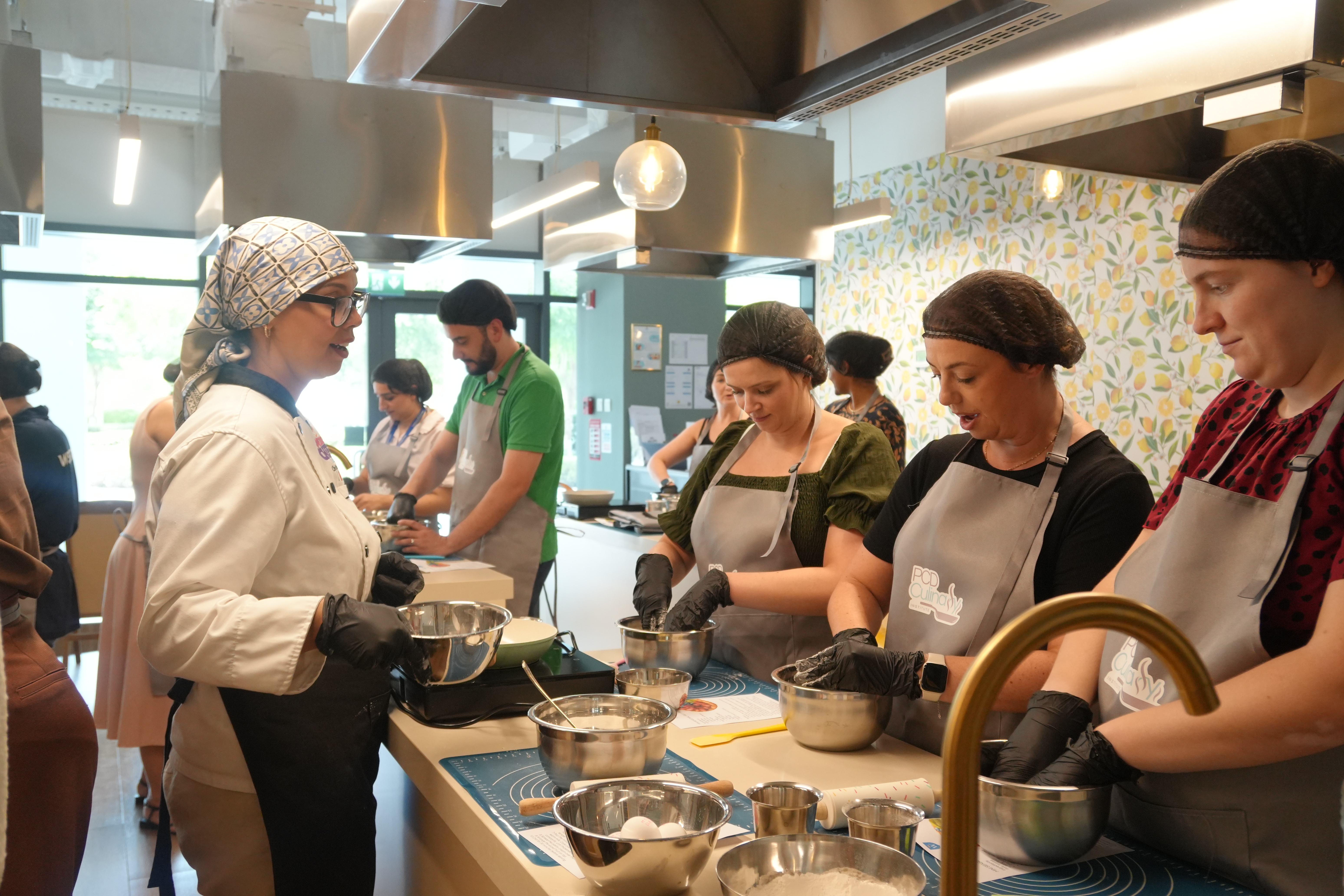 Adult students in PCD Culinary aprons working through a pastry session with the chef at the institute